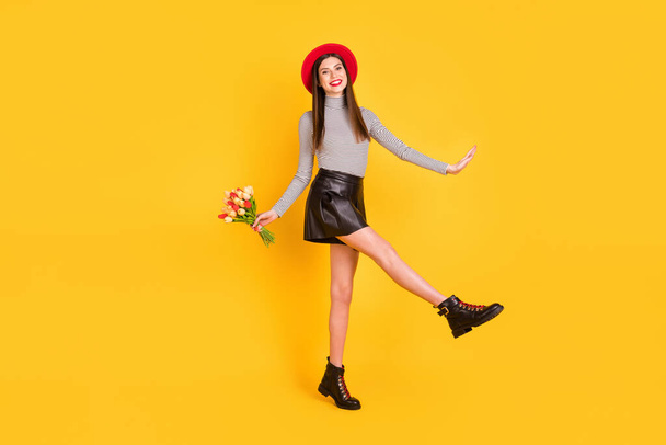 Photo of charming girlish young lady dressed glamour shirt holding tulips bunch walking isolated yellow color background - Φωτογραφία, εικόνα