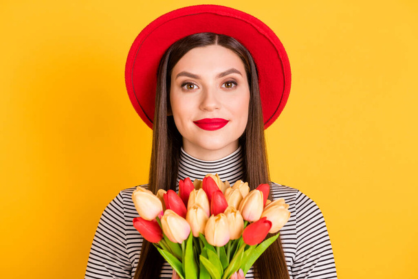 Photo of cute sweet young woman wear retro red hat hold hands tulip flowers isolated on yellow color background - Foto, Imagem