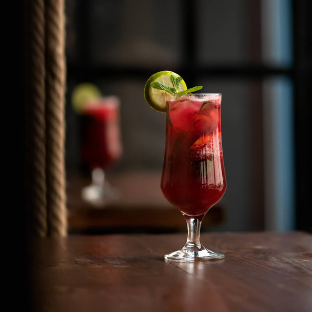 Стакан красного коктейля Алкогольный напиток с мятным листом и лимоном или ломтиком лимона на темном размытом фоне. Вид сбоку. Копирование пространства - Фото, изображение