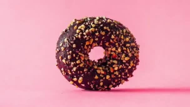 Donut de chocolate con almendras rematando girando acercándose y alejándose sobre fondo rosa. - Metraje, vídeo