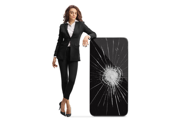 Full length portrait of a young businesswoman leaning on a cracked smartphone isolated on white background - Photo, Image