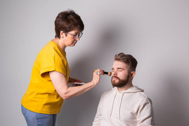 Bearded man getting makeup. Woman visagist works with brush. - Photo, Image