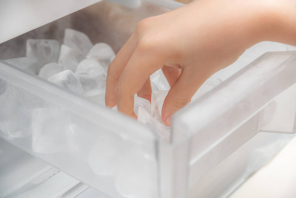 Dziewczyna wyciąga kostki lodu z maszyny do lodu, aby schłodzić wodę i napoje.. - Zdjęcie, obraz