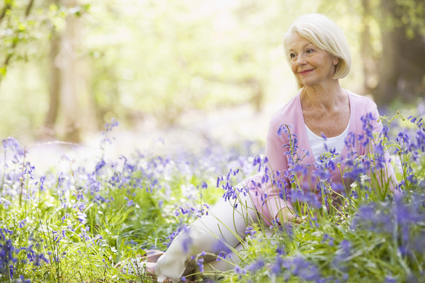 Nainen istuu ulkona kukat hymyillen
 - Valokuva, kuva