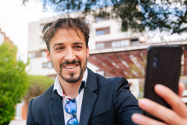 Adult businessman taking a selfie with his smart phone in the park near the office or workplace - Fotó, kép