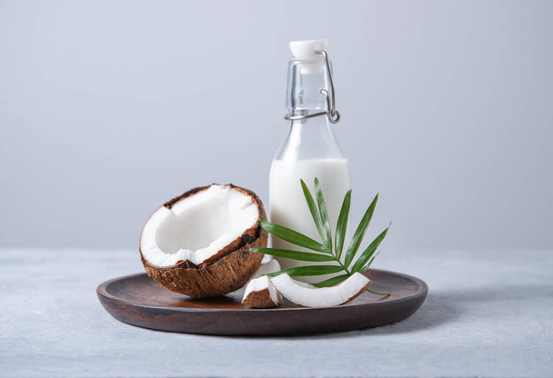 Botella de leche saludable con medio coco y rama de palma en plato de madera sobre fondo azul. Vista frontal y copia de imagen de espacio - Foto, imagen