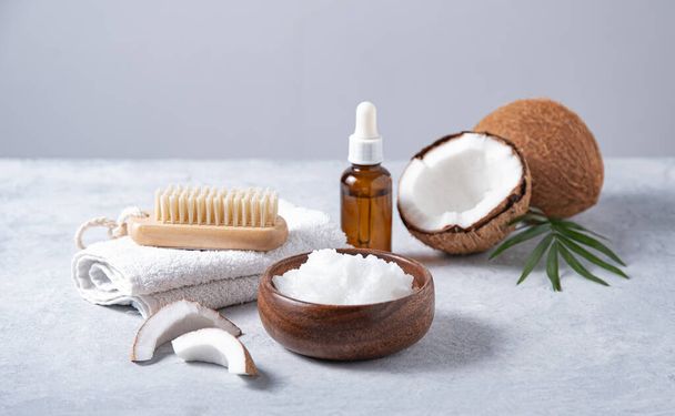 concept of organic spa. Healthy coconut oil with a wooden brush and half a coconut  on a blue background. Front view  image - Фото, изображение