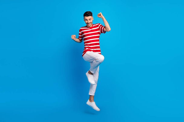 Full size photo of nice brunet hooray guy jump wear red t-shirt trousers sneakers isolated on vivid blue color background - Φωτογραφία, εικόνα