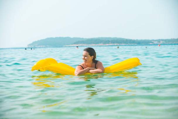 retrato de mujer bastante sonriente en colchón inflable amarillo en agua de mar azul - Foto, imagen