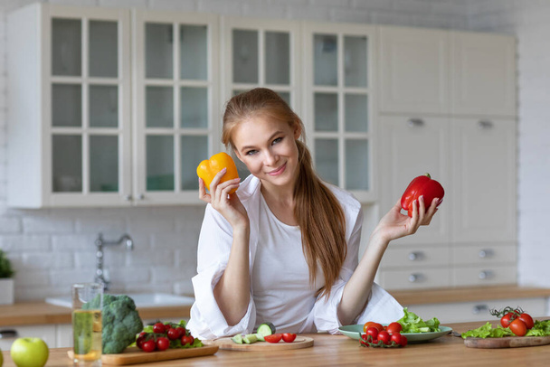 Vegetable food and diet - home lifestyle portrait smiling woman at domestic kitchen with fresh pepper. Stay healthy. - Photo, image