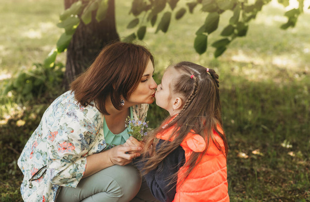 Young mother kisses her daughter in the park in the summer. concept of a happy family, the relationship of mother and child - Photo, image