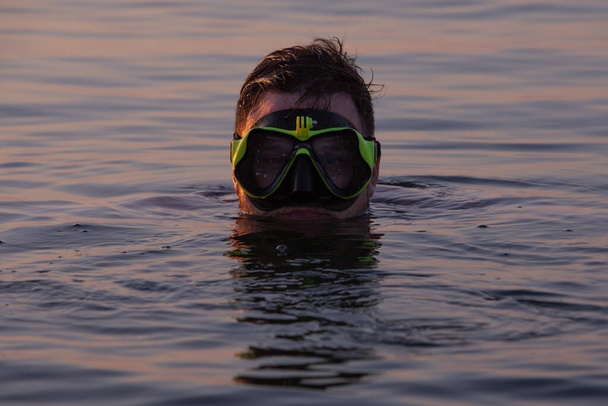 человек с маской для подводного плавания в воде на закате вблизи - Фото, изображение