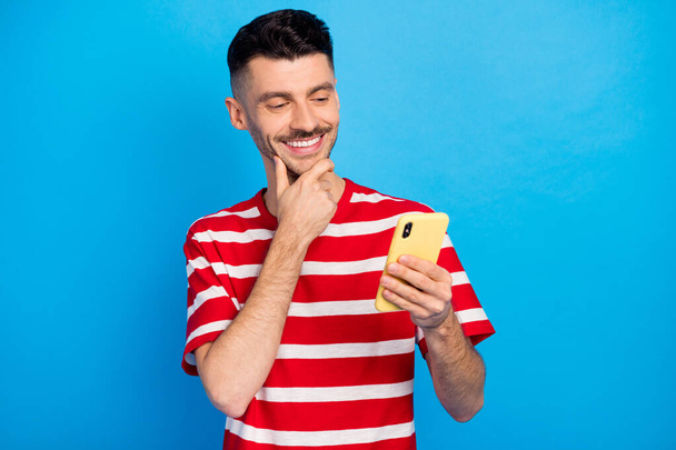 Photo of minded creative happy man look smartphone hold hand chin post comment isolated on blue color background - Photo, image