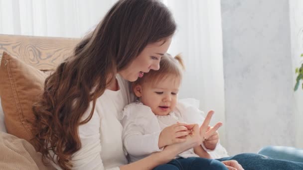 Happy caucasian young single mother woman babysitter mom takes care of hugging holding little cute baby daughter infant child playing game counts fingers shows hands gestures toddler enjoy motherhood - Footage, Video