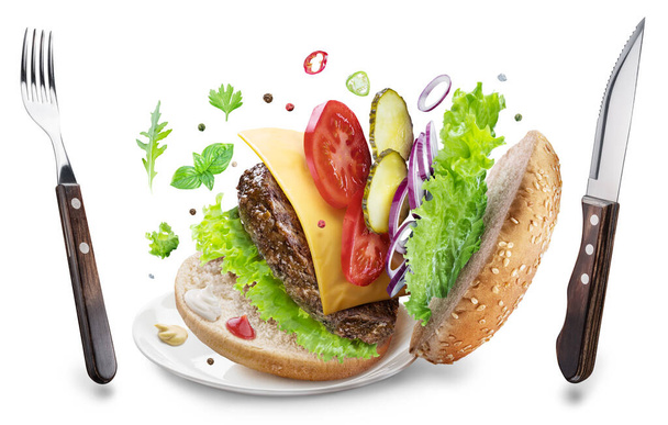 Cheeseburger ingredients and eating utensils hanging in the air. Conceptual picture of fast food. File contains clipping path. - Foto, imagen