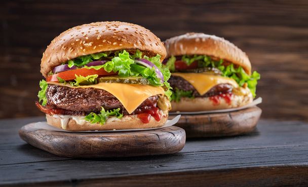 Delicious two hamburgers on a wooden table with a dark brown background behind. Fast food concept. - Valokuva, kuva