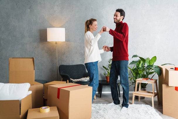 Portrait of a smiling couple moving together in a new house surrounded with boxes, dancing - Photo, image