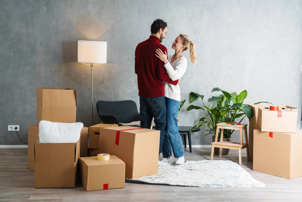 Portrait of a smiling couple moving together in a new house surrounded with boxes, dancing - Valokuva, kuva
