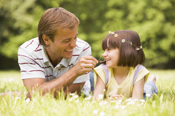 Father and daughter lying outdoors with flowers smiling - 写真・画像