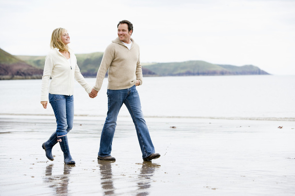 Couple walking on beach holding hands smiling - Foto, Bild