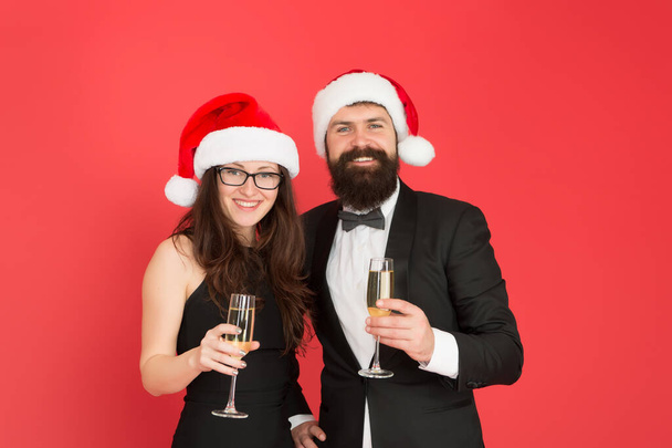 Sincere greetings. Merry christmas. Office party. Couple at corporate party. Happy new year. Bearded businessman in tuxedo and girl elegant dress drinking sparkling wine red background. Winter party - Photo, Image