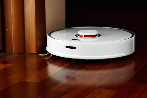 Smart Robot Vacuum Cleaner on wood floor. Robot vacuum cleaner performs automatic cleaning of the apartment at a certain time. Smart home - Photo, image
