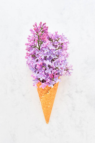 Waffle ice cream cone with pink lilac blossom flowers on a white marble background. Spring concept - Zdjęcie, obraz
