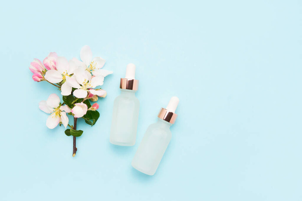 Two glass dropper bottles for medical and cosmetic use and apple tree blossom flowers on a light blue background - Foto, afbeelding
