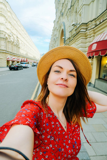 красива молода жінка в червоній сукні і солом'яному капелюсі посміхається і насолоджується прогулянкою по місту. портрет чистої шкіри крупним планом. літній туризм, радість від прогулянок
 - Фото, зображення