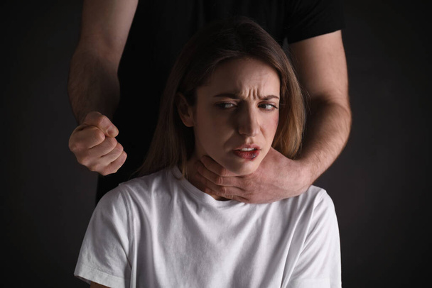 Man abusing scared woman on black background. Domestic violence - Fotoğraf, Görsel