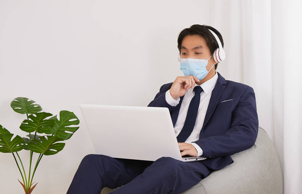 Azjatycki doradca finansowy nosić maskę i słuchawki Poważne myślenie przodu Laptop w Home Cafe Office. Biznesmen Praca na odległość społeczną lub kwarantanny domowej w Covid 19 lub sytuacji Coronavirus - Zdjęcie, obraz