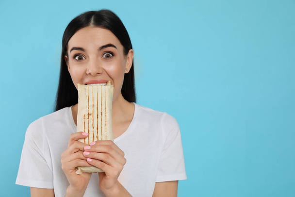 Young woman eating delicious shawarma on light blue background. Space for text - Photo, Image