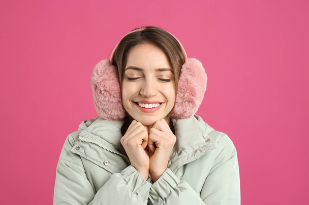 Happy woman wearing warm earmuffs on pink background - Fotoğraf, Görsel