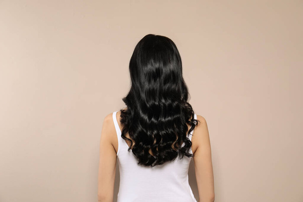 Young woman with long curly hair on beige background, back view - Foto, afbeelding