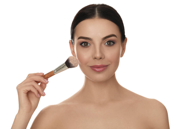 Beautiful young woman applying face powder with brush on white background - Valokuva, kuva