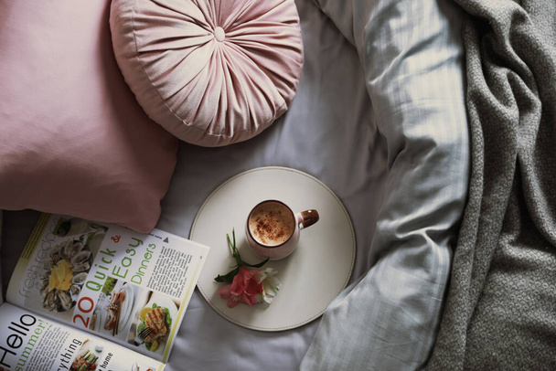 Aromatic coffee, magazine and beautiful flowers on bed with fresh linens, top view - 写真・画像