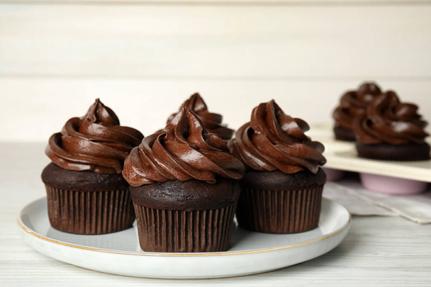 Plate with delicious chocolate cupcakes on white wooden table - Fotó, kép