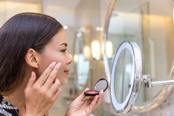 Asian woman putting blush looking in makeup mirror - Foto, immagini