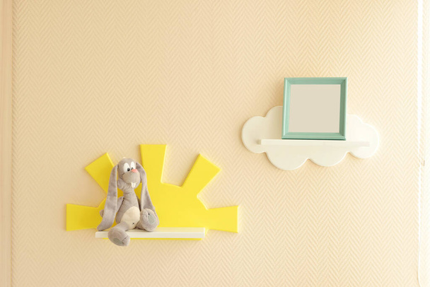Κομψός και μοντέρνος εσωτερικός σχεδιασμός. Σπίτι για το παιδικό δωμάτιο. Παιδικά ράφια με τη μορφή λευκών νεφών σε απλό μπεζ τοίχο με κορνίζα και γκρι λαγό - Φωτογραφία, εικόνα