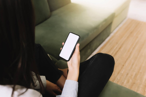 Koncepcja komunikacji z czarną dziewczyną słyszącą siedzącą na zielonej sofie i trzymającą smartfona w ręku z pustym białym ekranem, promieniami słońca z przodu - Zdjęcie, obraz