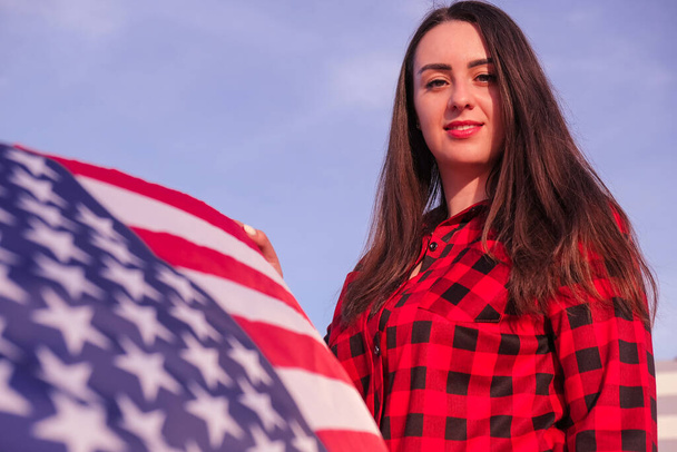 Young millennial brunette woman holding The National Flag of USA. American Flag. Tourist traveler or patriotism. Immigrant in free country. July 4th Independence Day. Caucasian - Фото, изображение