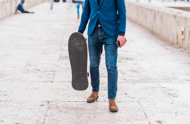 Fashionable guy taking a walk by river bridge while holding a skateboard - Photo, image