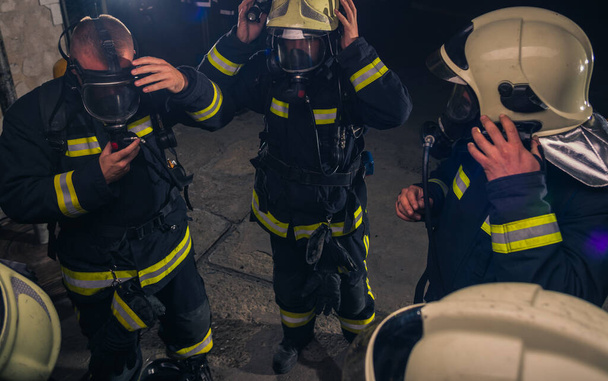 Grupo de bombeiros em pé dentro da brigada de incêndio usando capacete e uniforme de proteção - Foto, Imagem