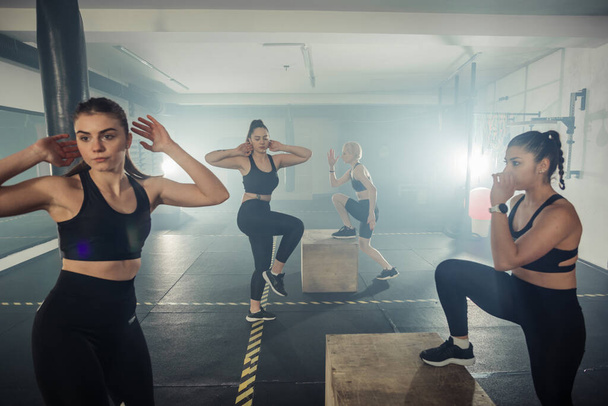 İşlevsel fitness eğitimi alan bir kadın grubu ayakta mekik çekiyor ve spor salonuna katılıyor. - Fotoğraf, Görsel
