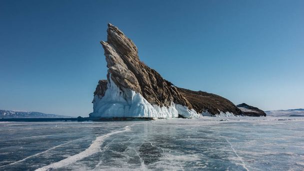 Une île rocheuse pittoresque dépourvue de végétation s'élève au milieu d'un lac gelé. Bizarre contours, hauts pointus, glaçons à la base. Il y a des fissures dans la glace. Ciel bleu clair. Baïkal - Photo, image