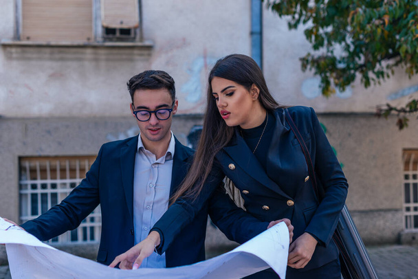 Business male and female architects looking at the blueprint about a building project outdoors. - Photo, image
