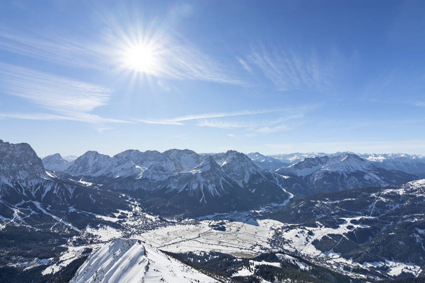 Vista desde la cima de una montaña hasta el valle de Ehrwald en un hermoso día en invierno. Paisaje alpino nevado salvaje con sol y cielo azul. Tirol, Austria - Foto, imagen