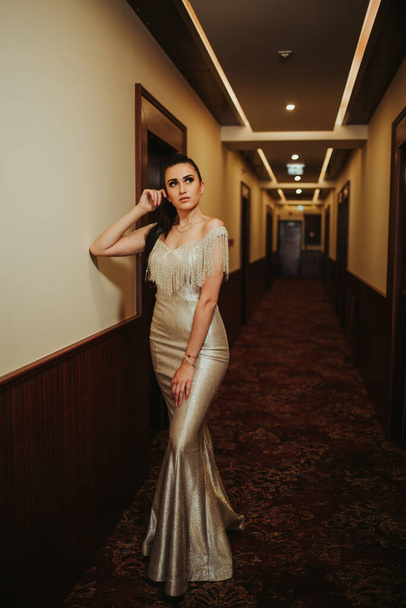 A vertical shot of a brunette female posing in a corridor in a gorgeous beige evening dress - Photo, Image