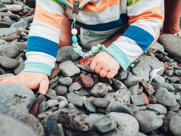 A closeup of a Caucasian baby playing with rocks on the seaside during daylight - Foto, Imagen