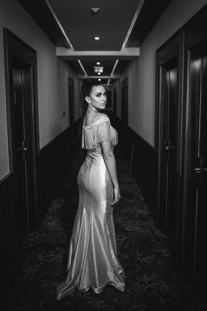 A vertical grayscale shot of a beautiful Caucasian female in an elegant dress posing in a corridor - Foto, immagini
